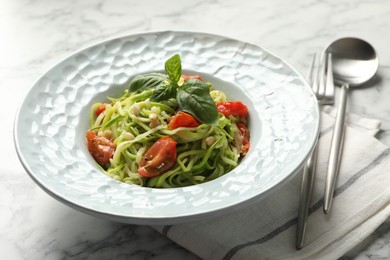 Photo of Tasty zucchini noodles with tomatoes, pine nuts and basil served on white marble table, closeup