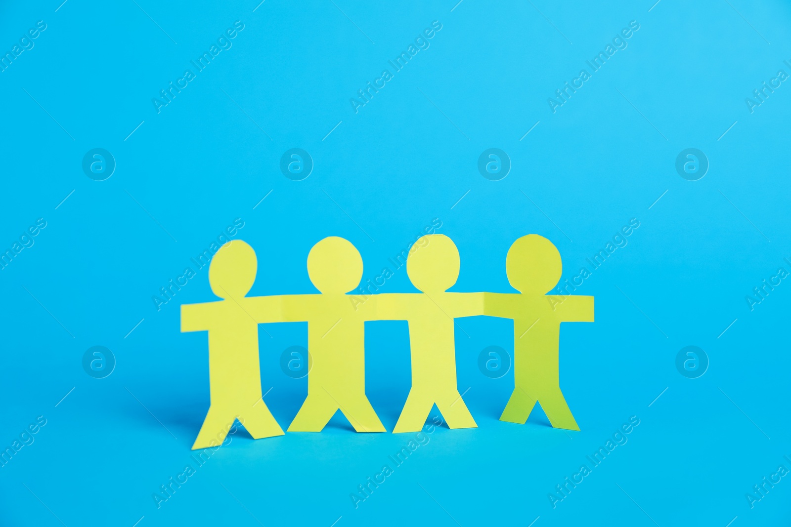 Human paper figures holding hands on light blue background Photo of Human paper figures holding hands on light blue background
