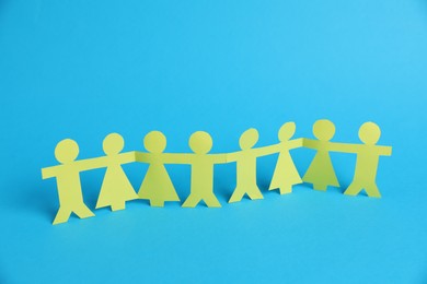 Photo of Human paper figures holding hands on light blue background