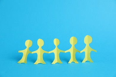 Photo of Human paper figures holding hands on light blue background