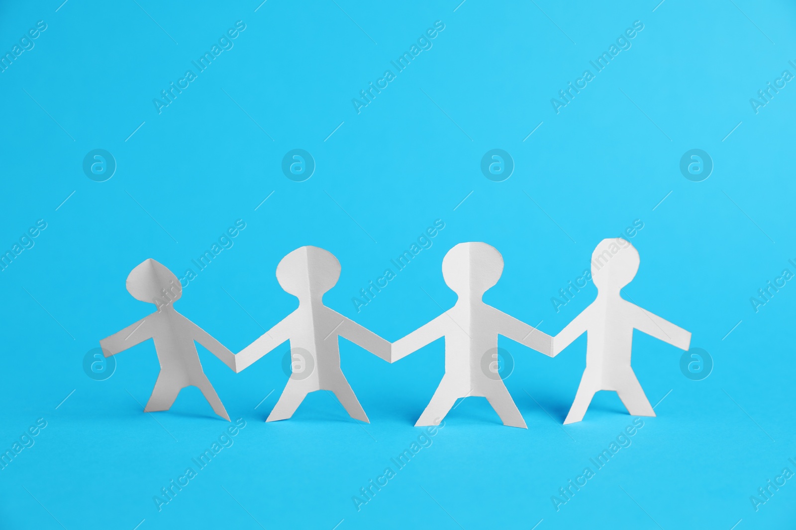 Photo of Human paper figures holding hands on light blue background