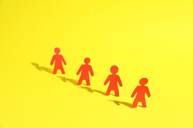 Photo of Many human paper figures on yellow background. Space for text