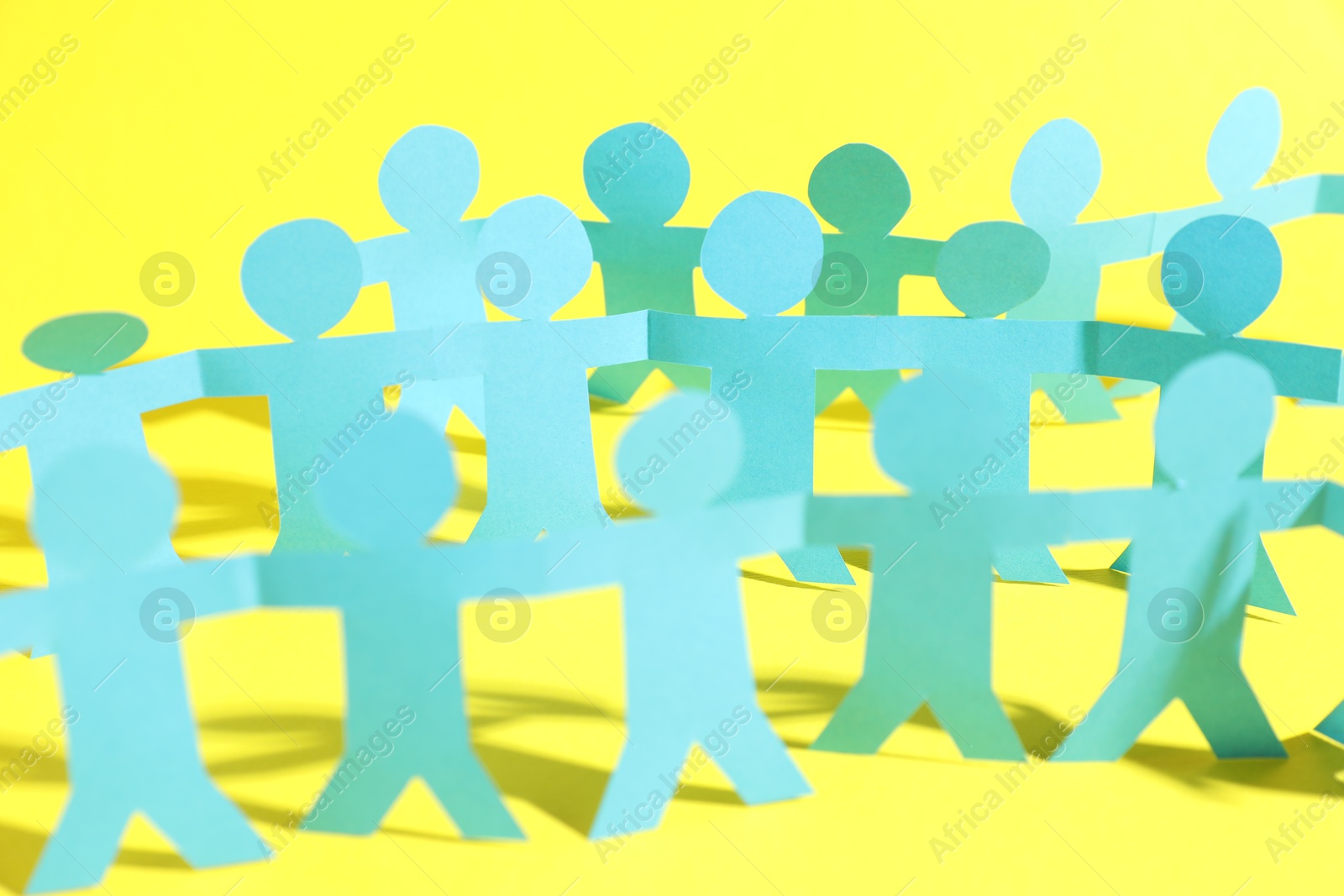 Photo of Human paper figures holding hands on yellow background, closeup
