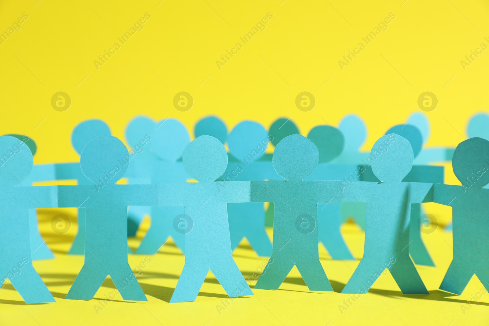 Human paper figures holding hands on yellow background, closeup Photo of Human paper figures holding hands on yellow background, closeup