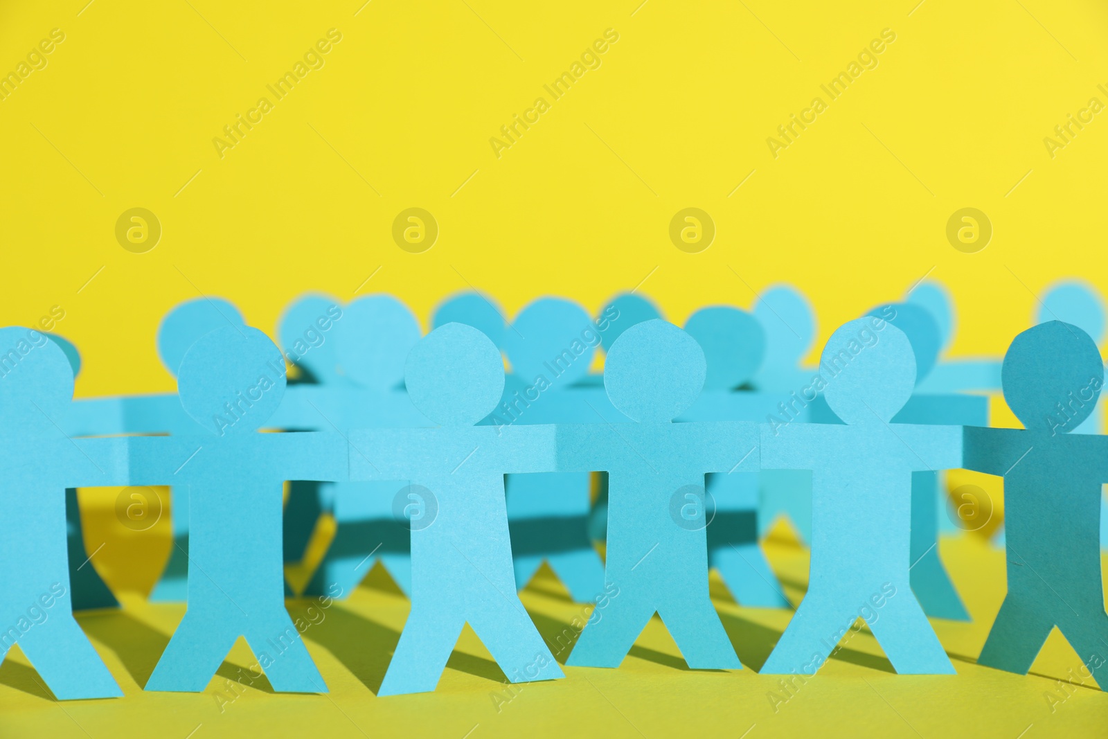 Human paper figures holding hands on yellow background, closeup Photo of Human paper figures holding hands on yellow background, closeup