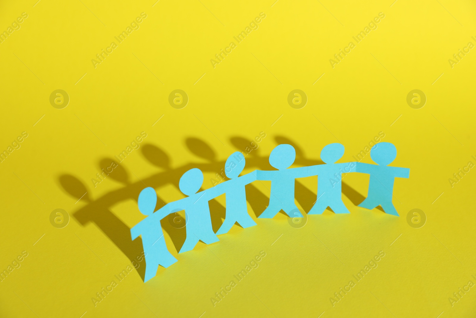 Photo of Human paper figures holding hands on yellow background