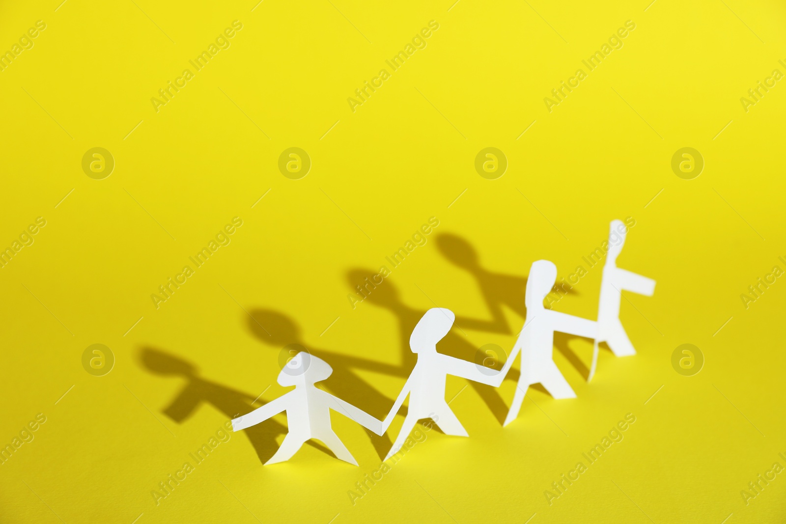 Human paper figures holding hands on yellow background. Space for text Photo of Human paper figures holding hands on yellow background. Space for text