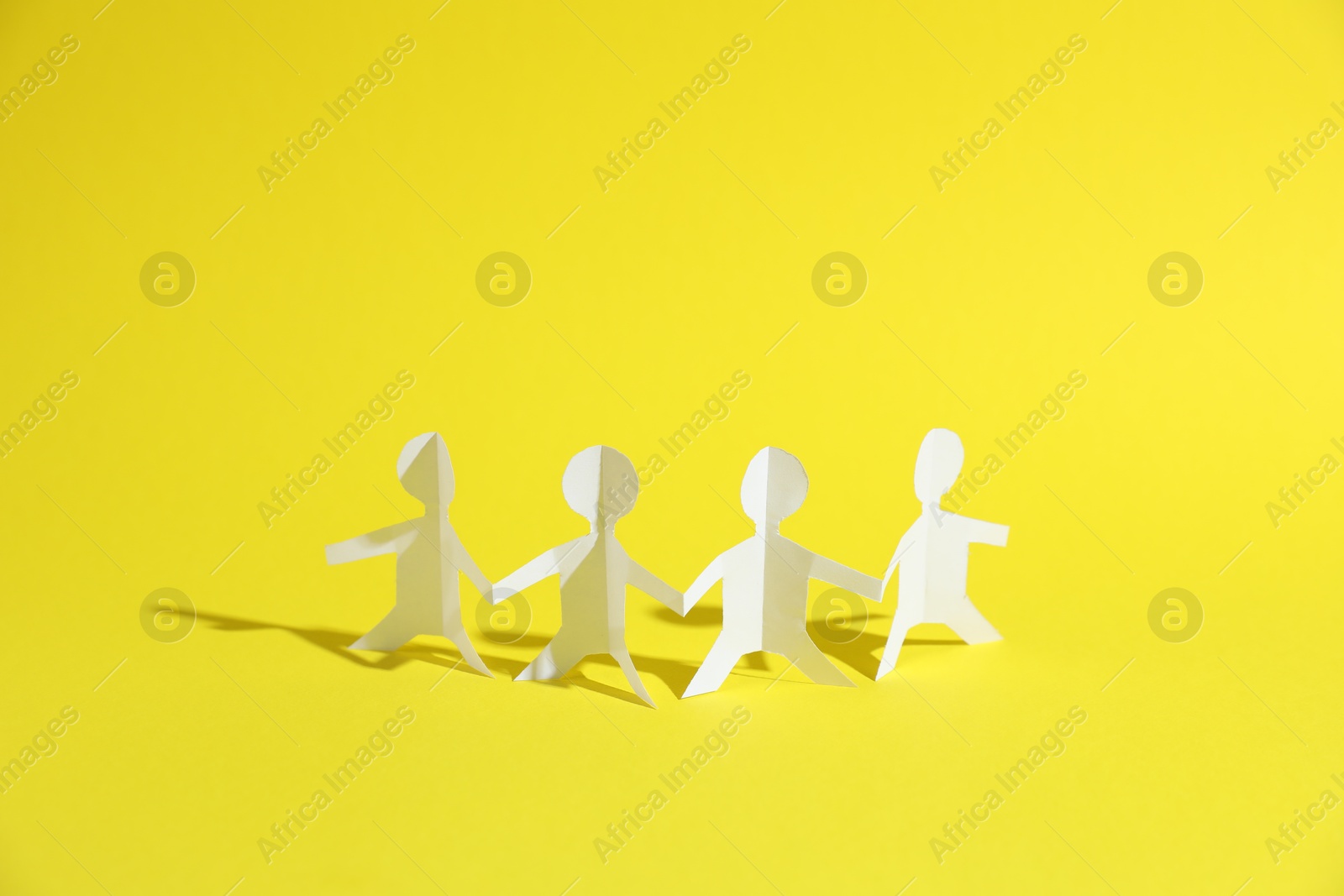 Human paper figures holding hands on yellow background Photo of Human paper figures holding hands on yellow background