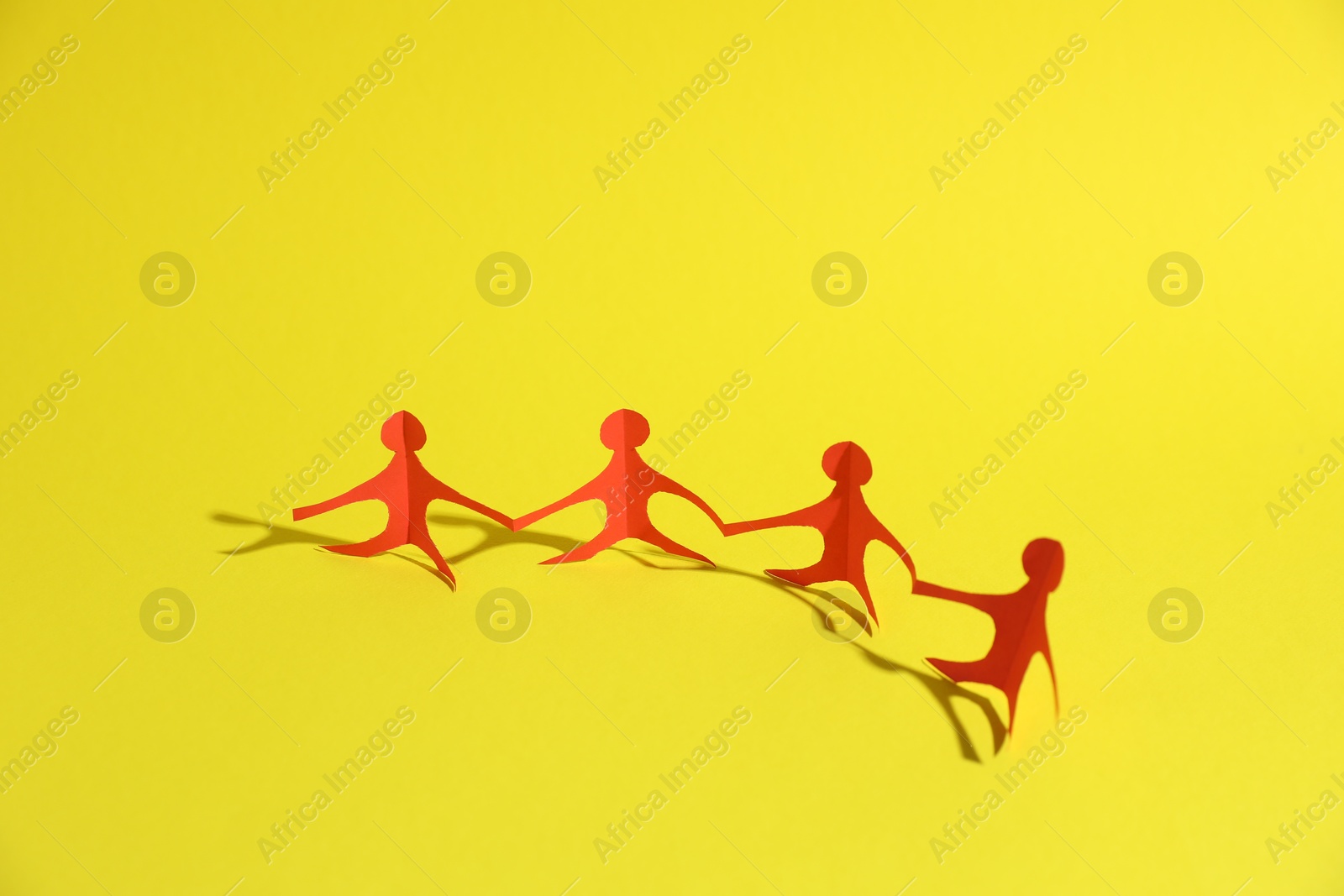 Human paper figures holding hands on yellow background Photo of Human paper figures holding hands on yellow background