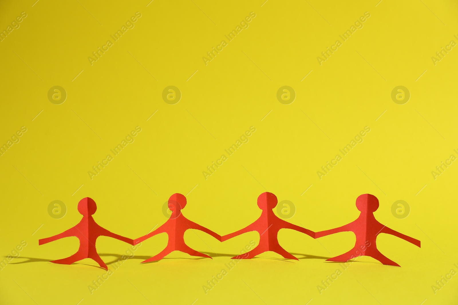 Human paper figures holding hands on yellow background. Space for text Photo of Human paper figures holding hands on yellow background. Space for text