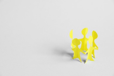 Photo of Human paper figures holding hands on light background. Space for text