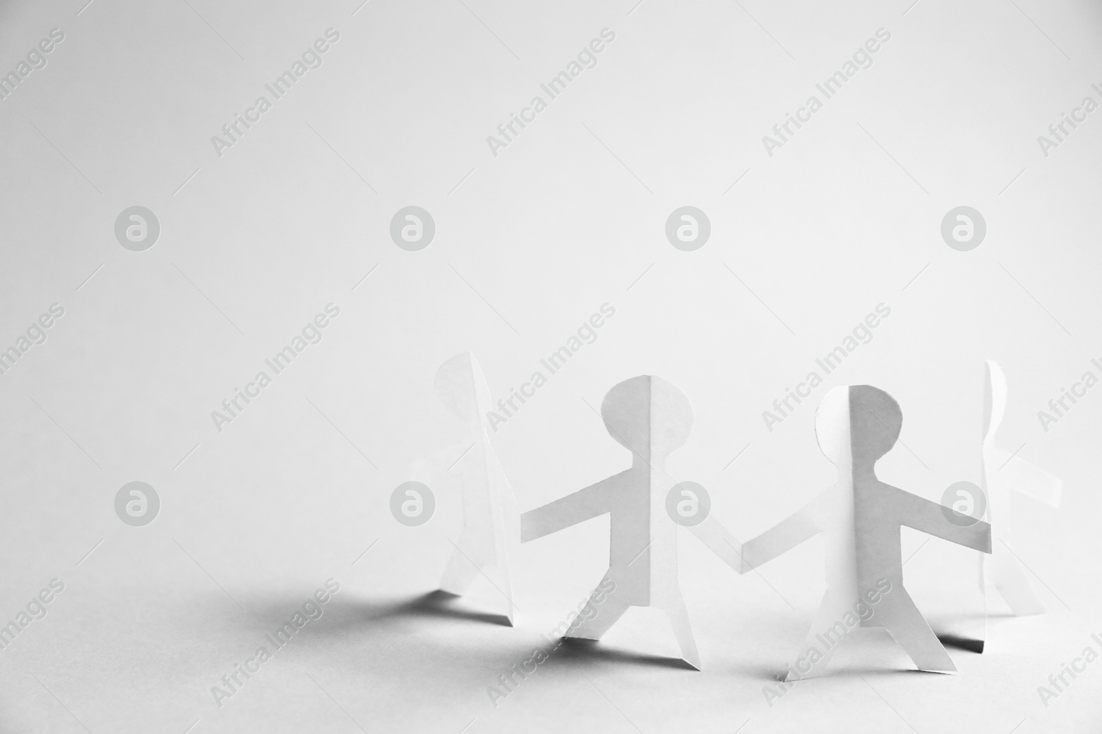 Human paper figures holding hands on light background. Space for text Photo of Human paper figures holding hands on light background. Space for text