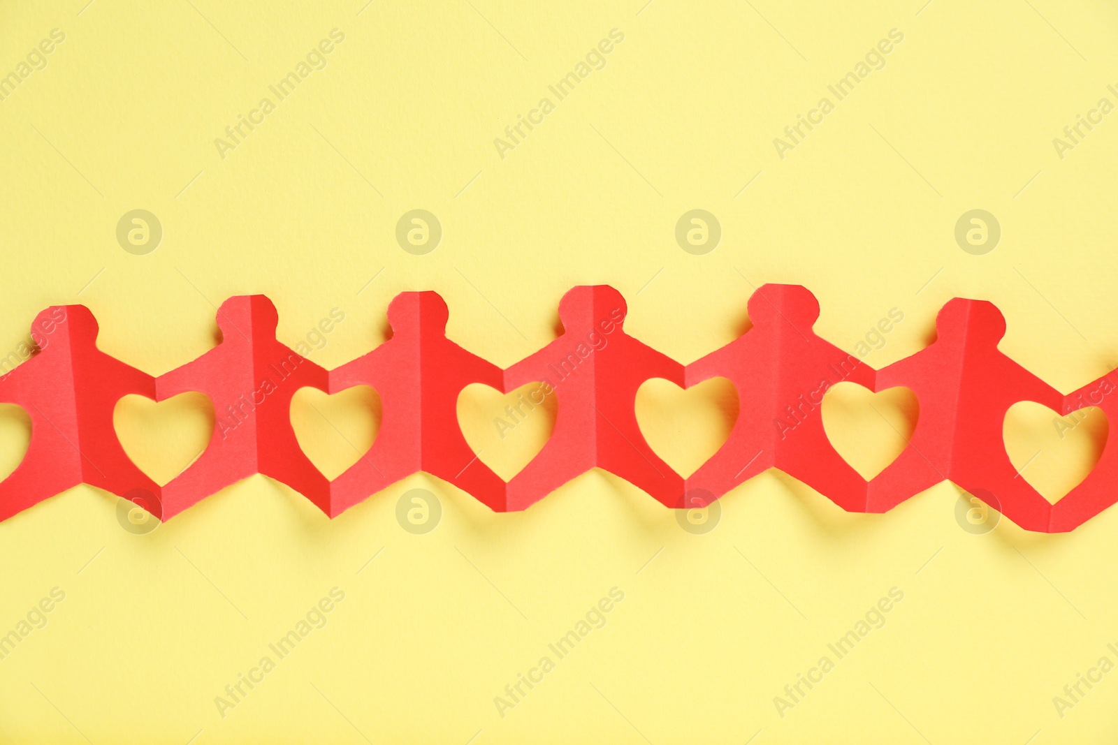 Photo of Human paper figures holding hands on yellow background, top view