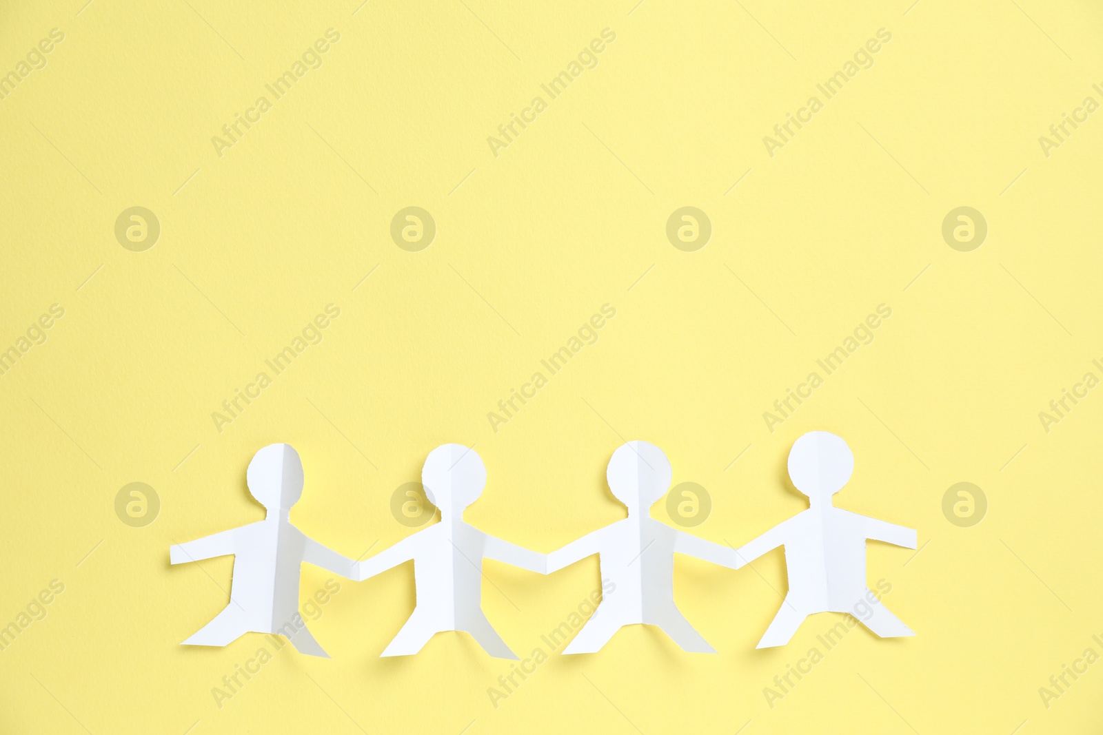 Human paper figures holding hands on yellow background, top view. Space for text Photo of Human paper figures holding hands on yellow background, top view. Space for text