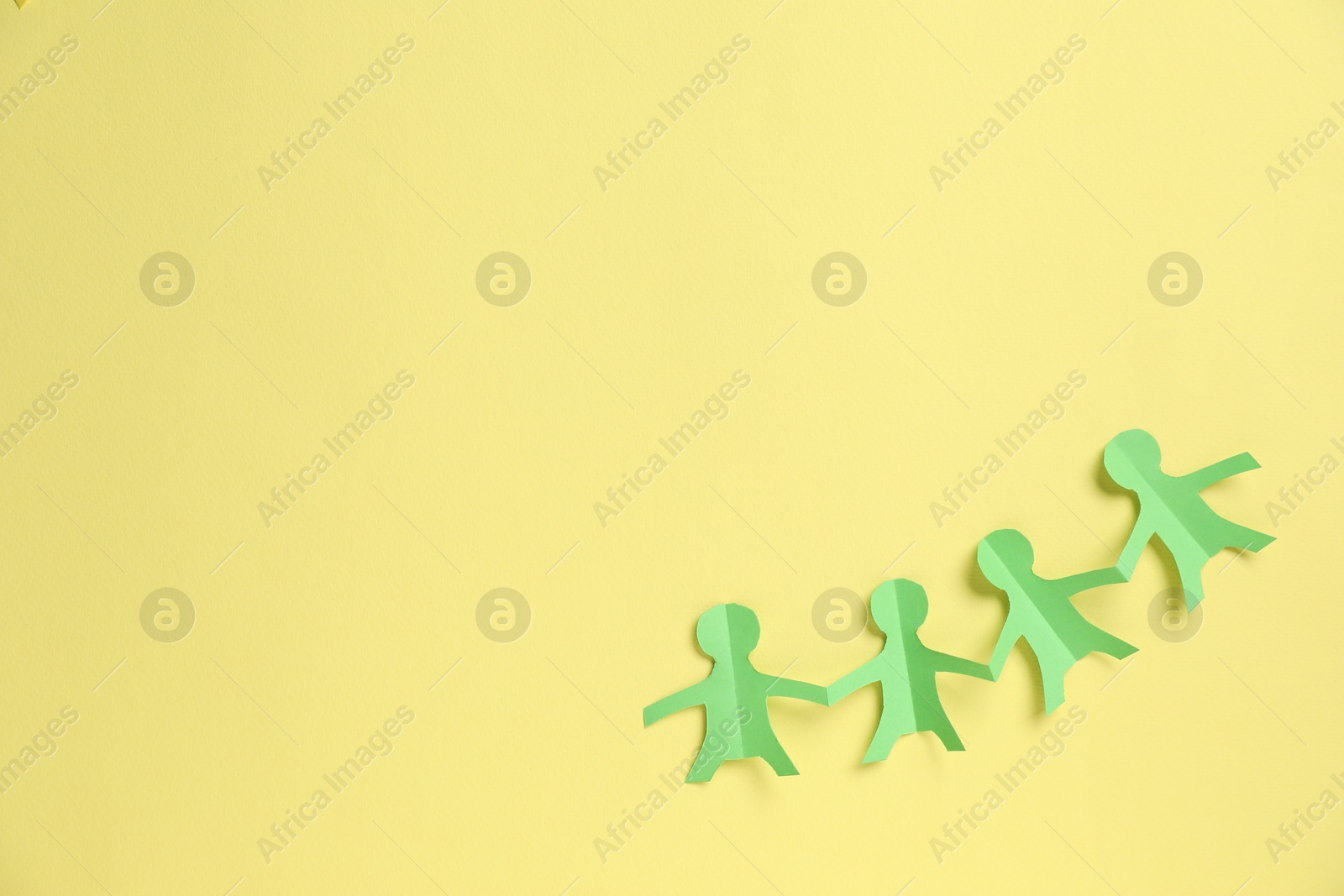 Photo of Human paper figures holding hands on yellow background, top view. Space for text
