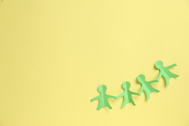 Photo of Human paper figures holding hands on yellow background, top view. Space for text