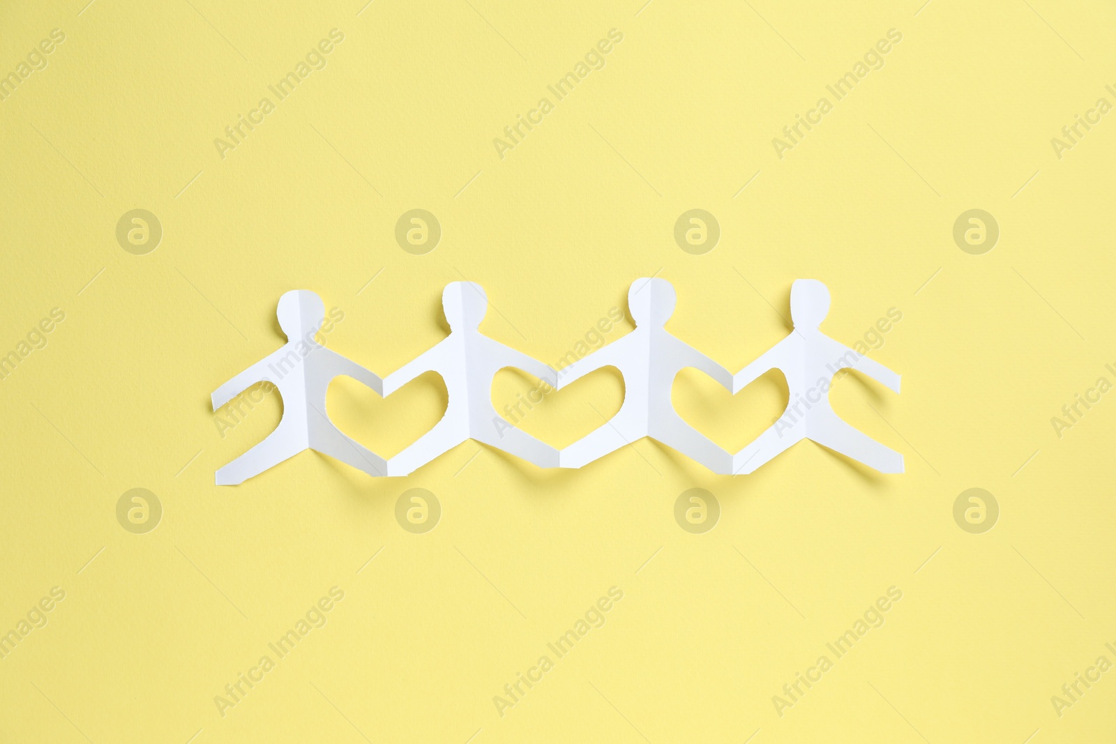 Human paper figures holding hands on yellow background, top view Photo of Human paper figures holding hands on yellow background, top view