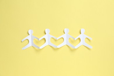 Photo of Human paper figures holding hands on yellow background, top view