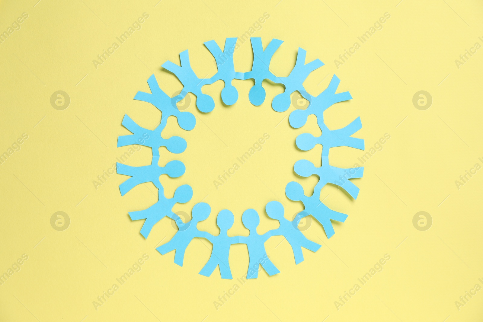 Human paper figures holding hands on yellow background, top view Photo of Human paper figures holding hands on yellow background, top view