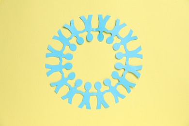 Photo of Human paper figures holding hands on yellow background, top view
