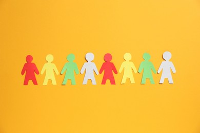 Photo of Many human paper figures on orange background, flat lay