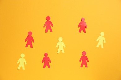 Photo of Many human paper figures on orange background, flat lay