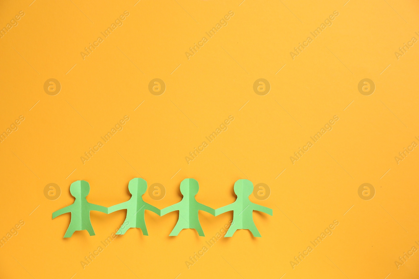 Human paper figures holding hands on orange background, top view. Space for text Photo of Human paper figures holding hands on orange background, top view. Space for text