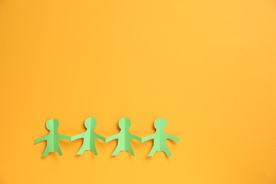 Photo of Human paper figures holding hands on orange background, top view. Space for text