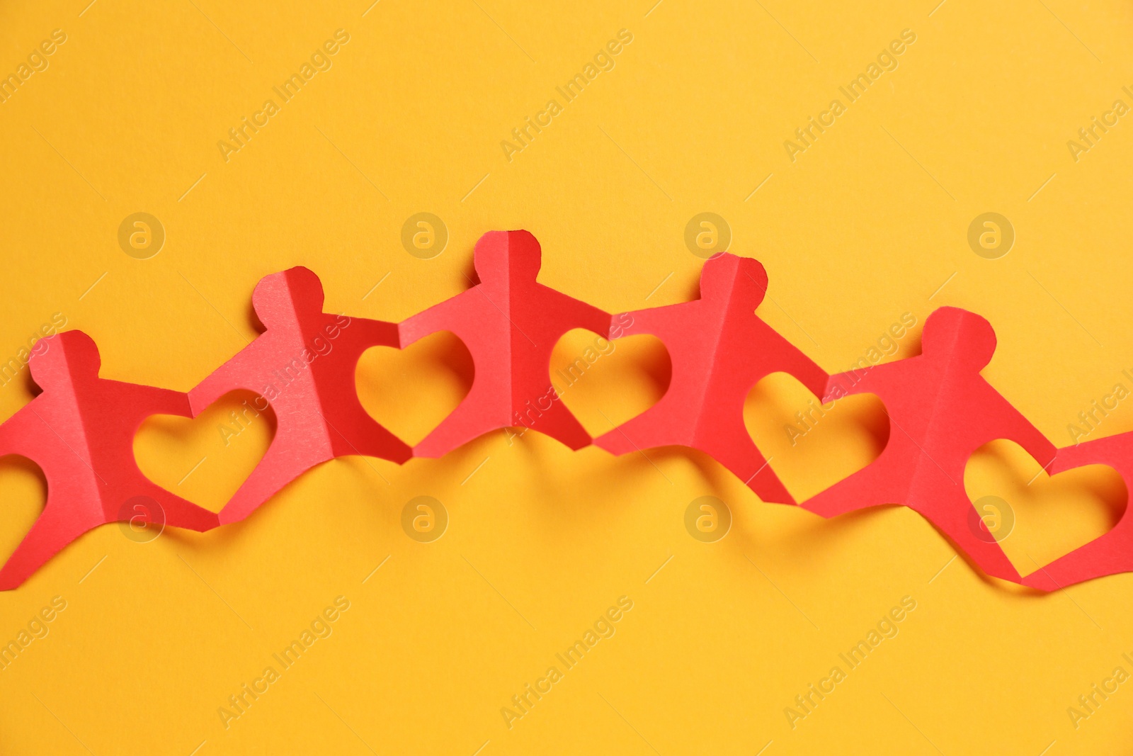 Human paper figures holding hands on orange background, top view Photo of Human paper figures holding hands on orange background, top view