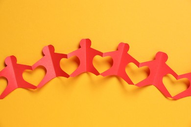 Photo of Human paper figures holding hands on orange background, top view