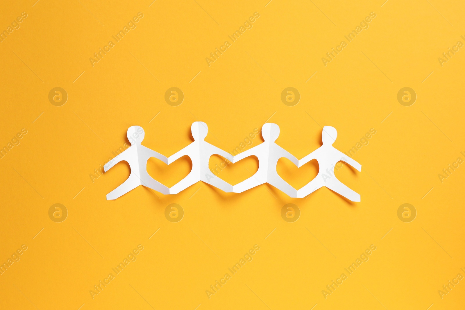 Human paper figures holding hands on orange background, top view Photo of Human paper figures holding hands on orange background, top view