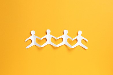 Photo of Human paper figures holding hands on orange background, top view