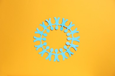 Photo of Human paper figures holding hands on orange background, top view