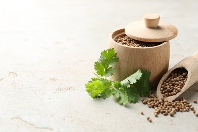 Photo of Coriander seeds and fresh cilantro sprig on light textured table, closeup. Space for text