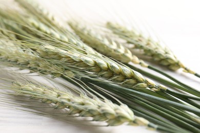 Photo of Many green wheat spikes on light wooden table, closeup