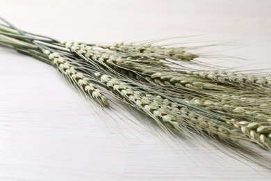 Photo of Many green wheat spikes on light wooden table, closeup