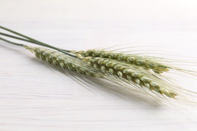 Photo of Green wheat spikes on light wooden table, closeup