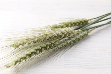 Photo of Green wheat spikes on light wooden table, closeup