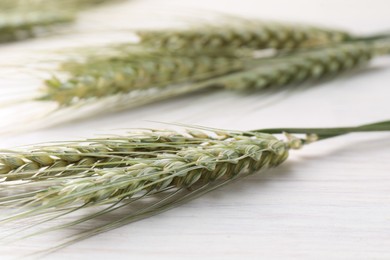 Photo of Many green wheat spikes on light wooden table, closeup