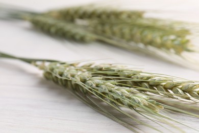 Photo of Many green wheat spikes on light wooden table, closeup