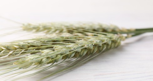 Photo of Green wheat spikes on light wooden table, closeup