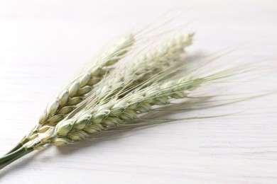 Photo of Green wheat spikes on light wooden table, closeup