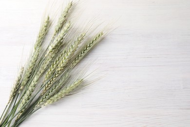 Photo of Many green wheat spikes on light wooden table, flat lay. Space for text