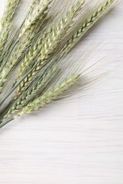 Photo of Many green wheat spikes on light wooden table, flat lay. Space for text