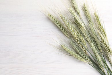 Photo of Many green wheat spikes on light wooden table, flat lay. Space for text