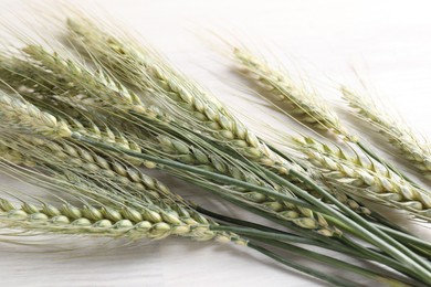 Photo of Many green wheat spikes on light wooden table, flat lay