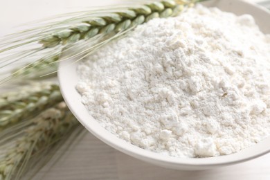 Photo of Green wheat spikes and flour on light wooden table, closeup