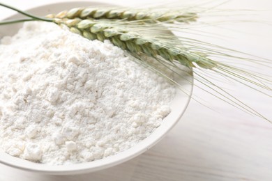 Photo of Green wheat spikes and flour on light wooden table, closeup