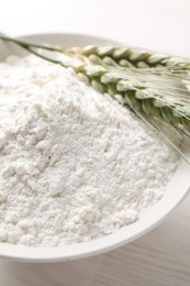 Photo of Green wheat spikes and flour on light wooden table, closeup