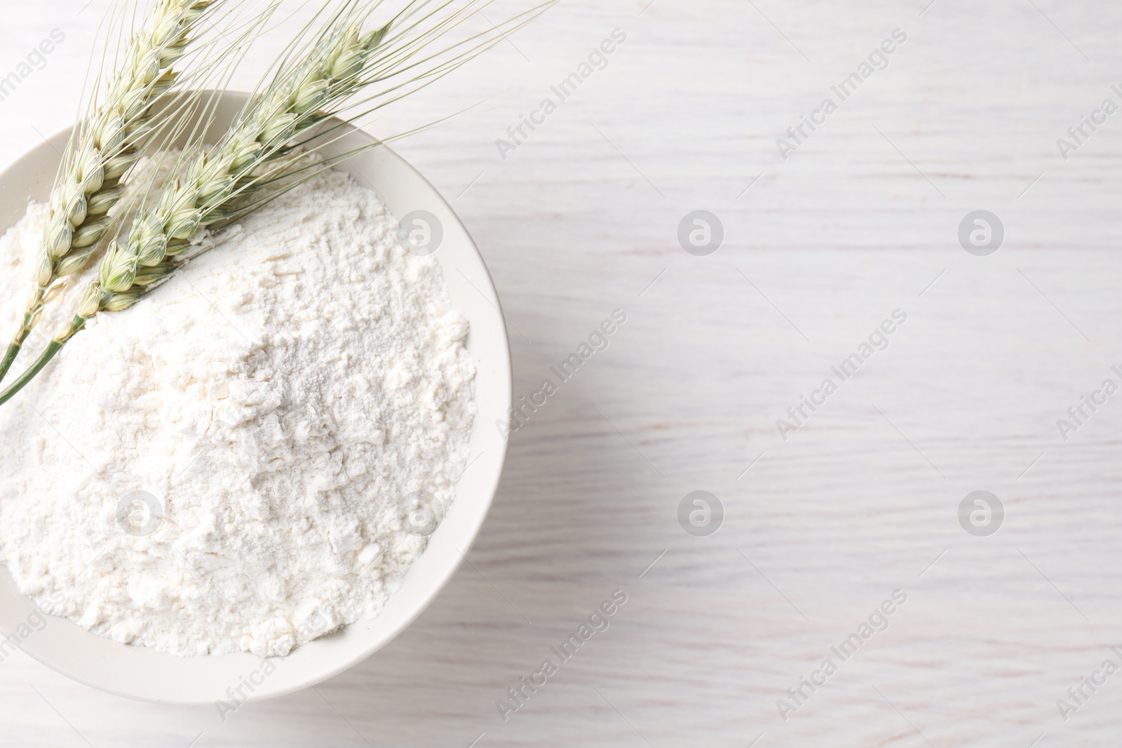 Green wheat spikes and flour on light wooden table, top view. Space for text Photo of Green wheat spikes and flour on light wooden table, top view. Space for text